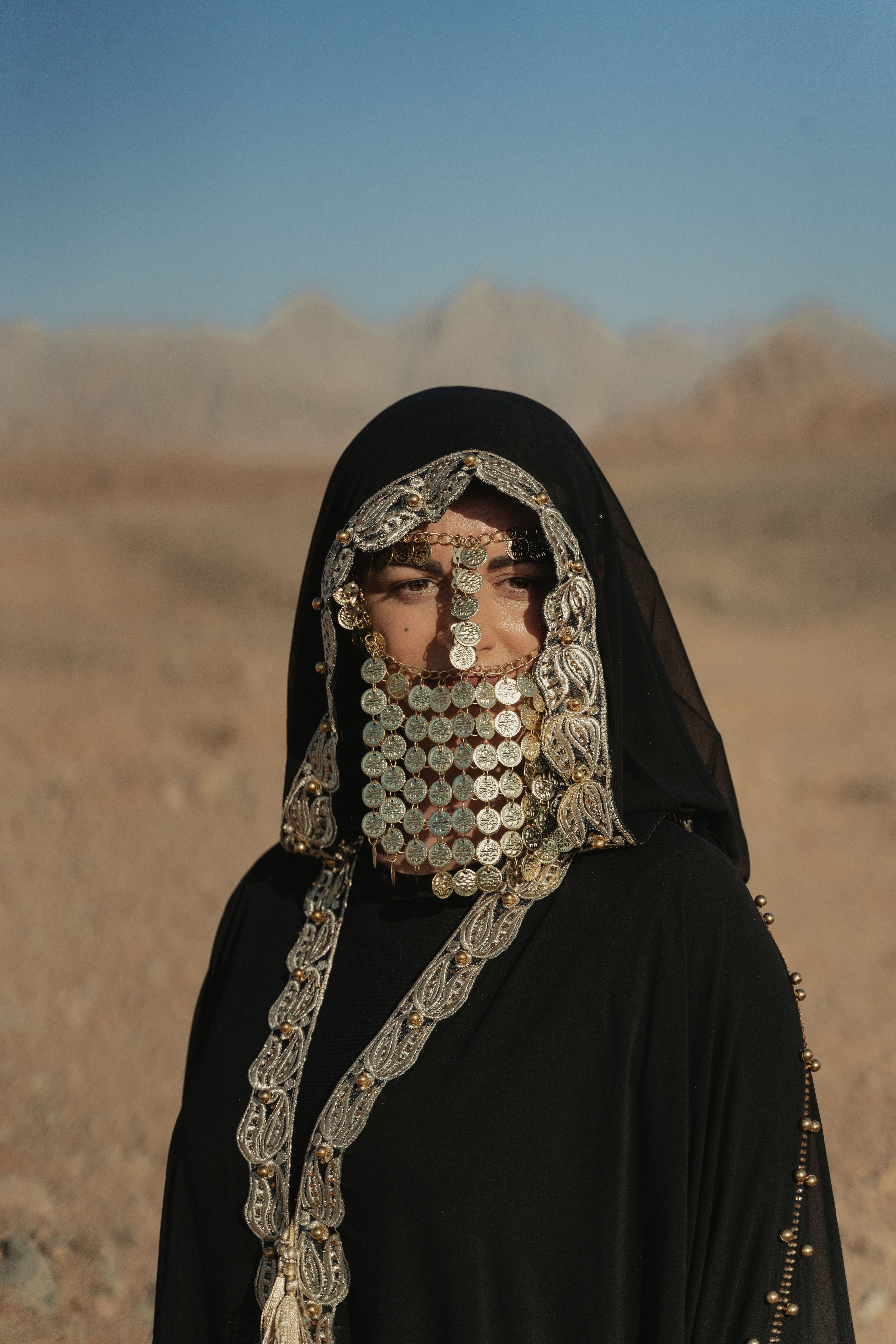 Woman wearing traditional Bedouin attire with coin jewelry in a desert landscape