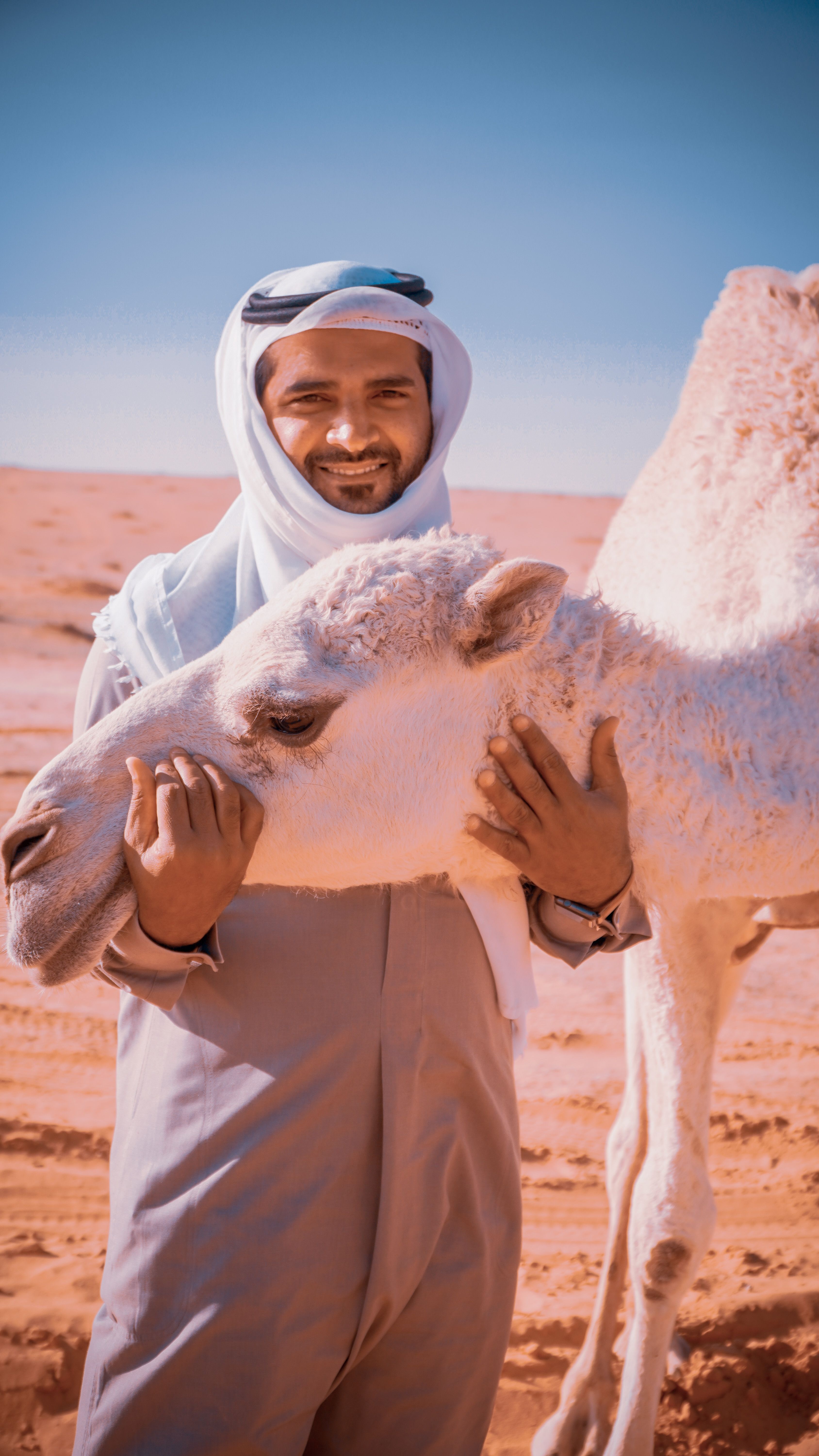 A happy man in traditional wear embracing his camel in a desert setting